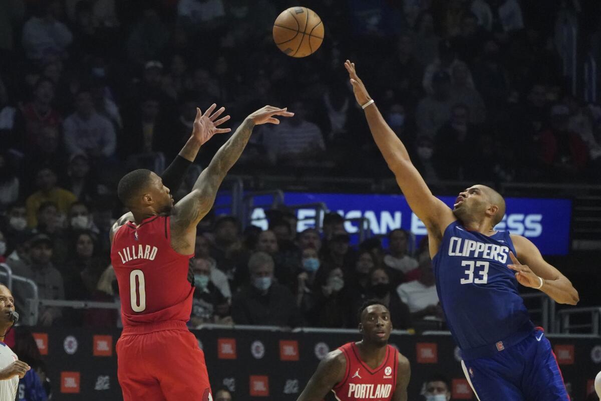 Clippers forward Nicolas Batum stretches his hand in the air to contest a shot by Trail Blazers guard Damian Lillard