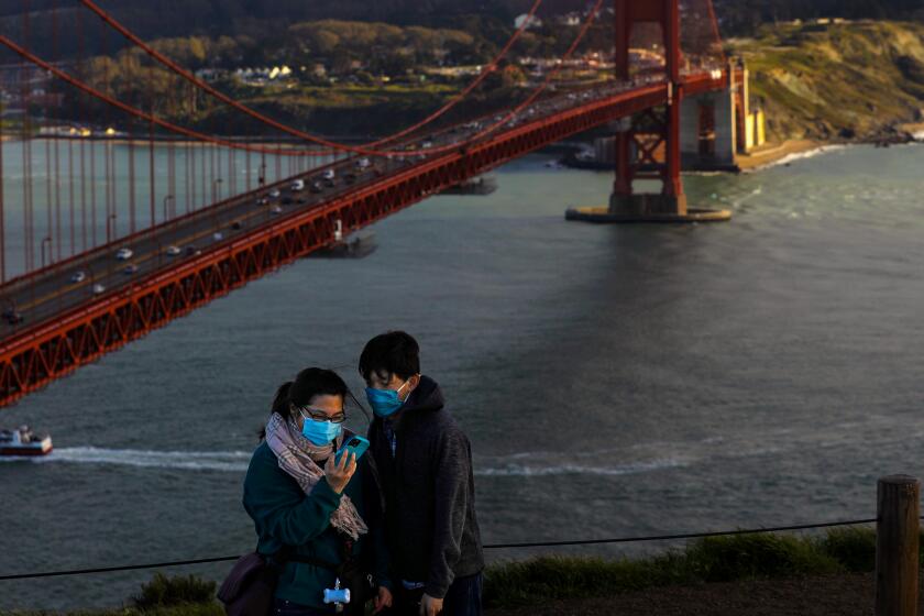 SAN FRANCISCO, CA - MARCH 13: People look at their selfie with the Golden Gate bridge in the background taken from Battery Spencer, former Fort Baker site, on Saturday, March 13, 2021 in San Francisco, CA. On March 2, 2021, the San Francisco Department of Public Health updated a COVID-19 health order to allow many businesses to reopen at the Red Tier. (Gary Coronado / Los Angeles Times)