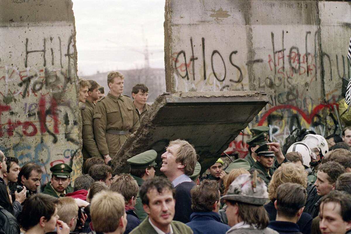 West Berliners crowd in front of the Berlin Wall as they watch East German border guards demolishing a section of the wall in order to open a new crossing point between East and West Berlin in 1989.