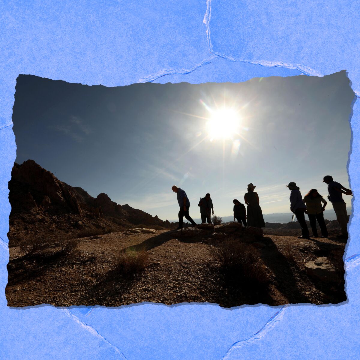 A group of people are seen on a hill in silhouette with the sun shining in the sky.