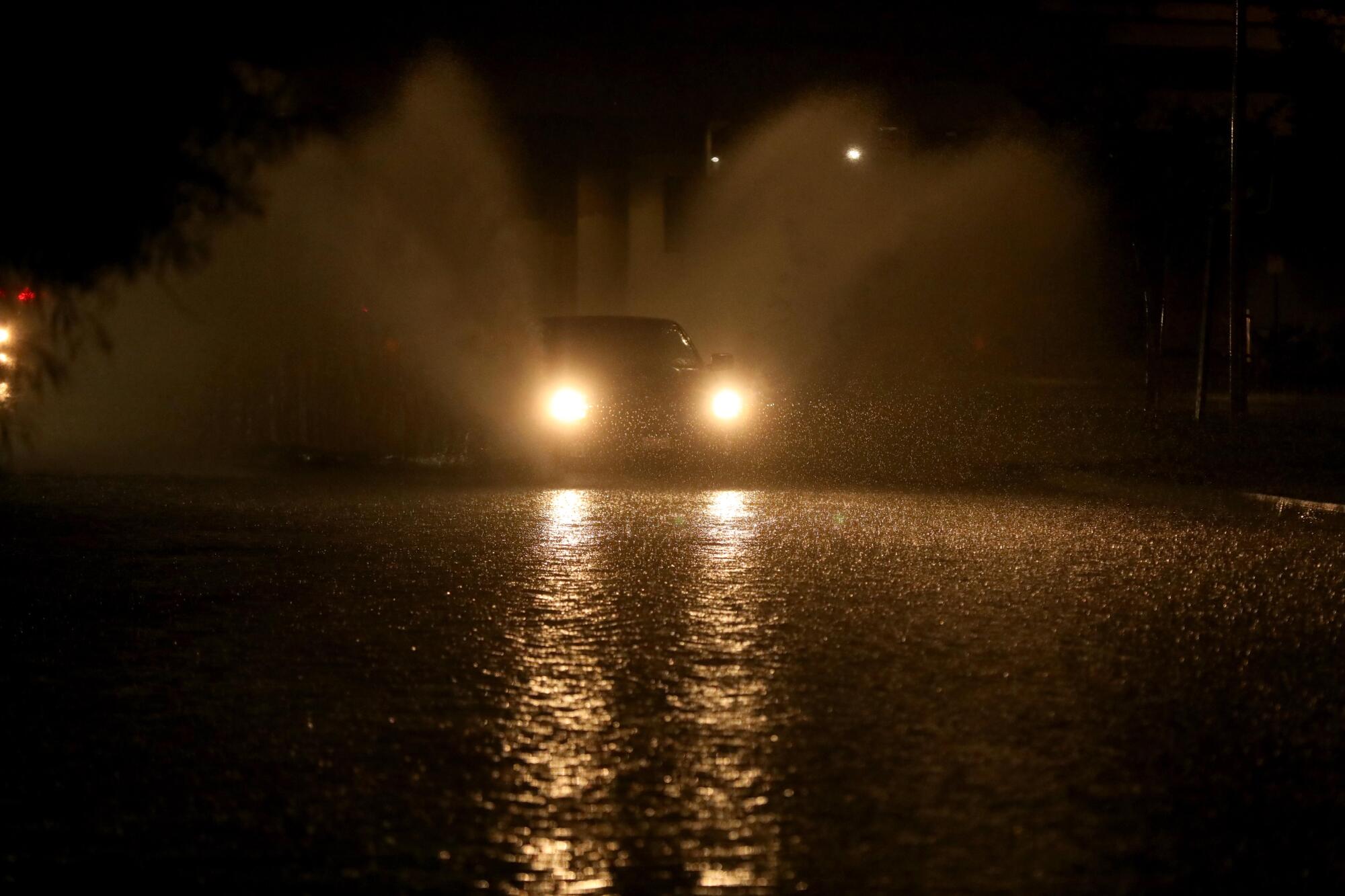 The headlights of a vehicle illuminate a flooded street 