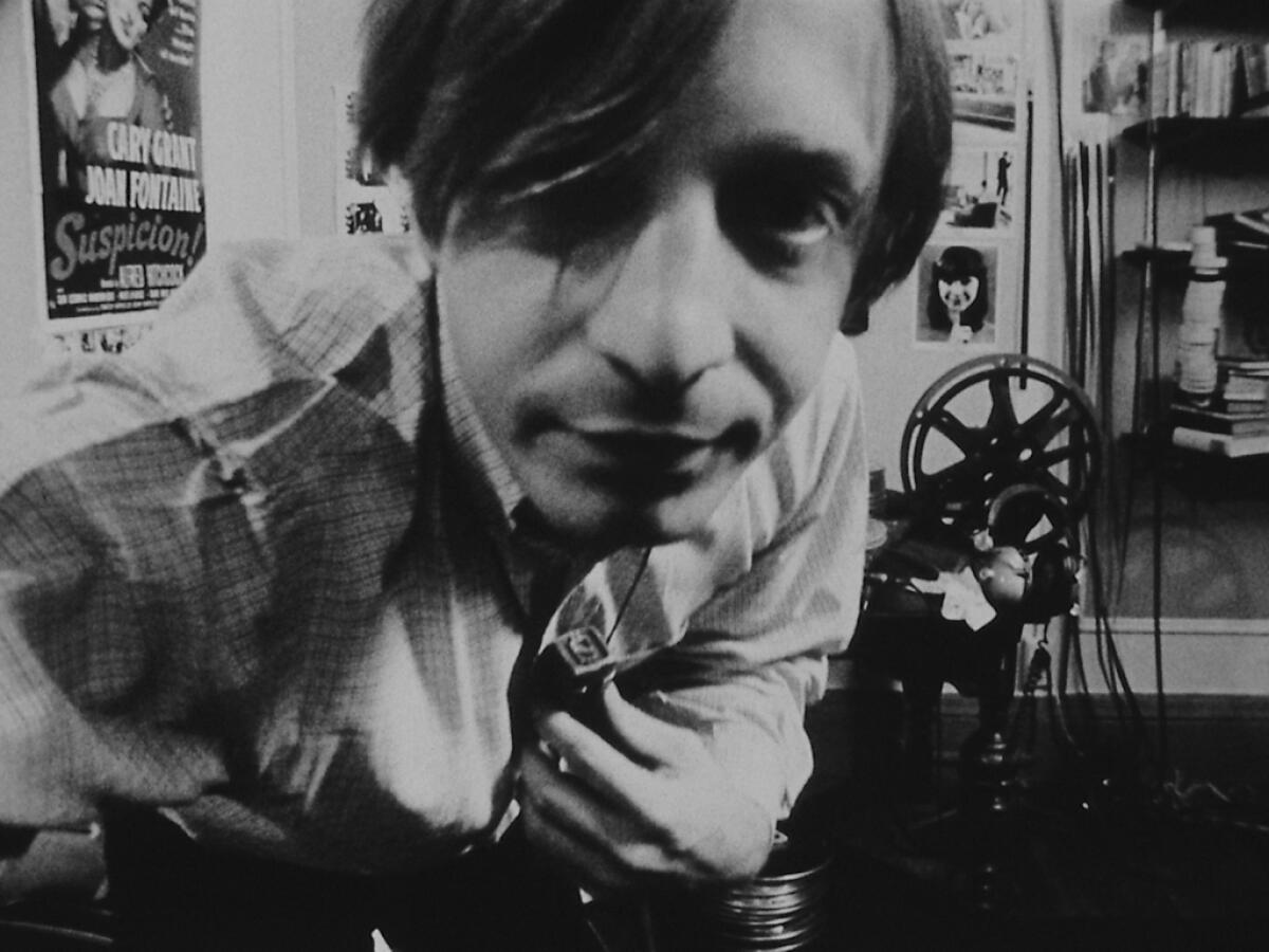 Sitting in front of a film projector, a man peers closely into the lens.
