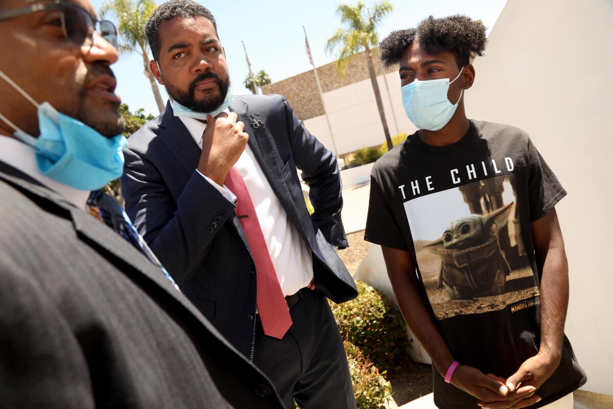 A young Black man wearing a mask stands next to his attorneys at a news conference