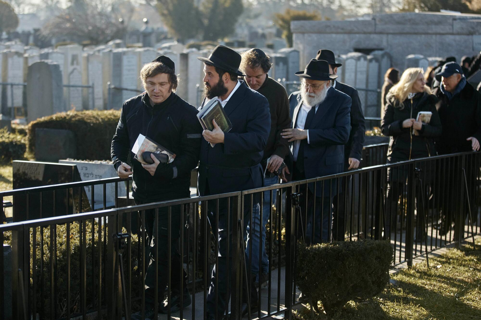 Several people, some dressed as Orthodox Jews, walk in a cemetery