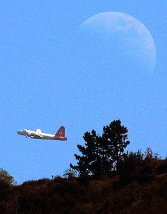 An air tanker passes under a rising moon while fighting the Morris fire.