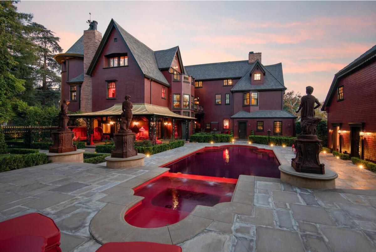 A red Victorian house overlooks a slate patio with a blood-red swimming pool