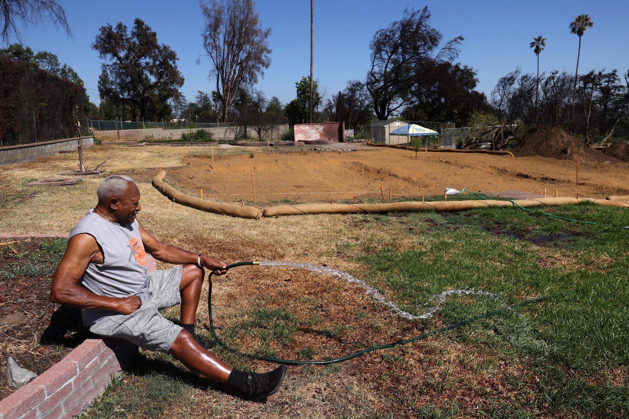 Walt "The Jet" Butler, a longtime Altadena resident, waters his lawn against a backdrop of where his house once stood.