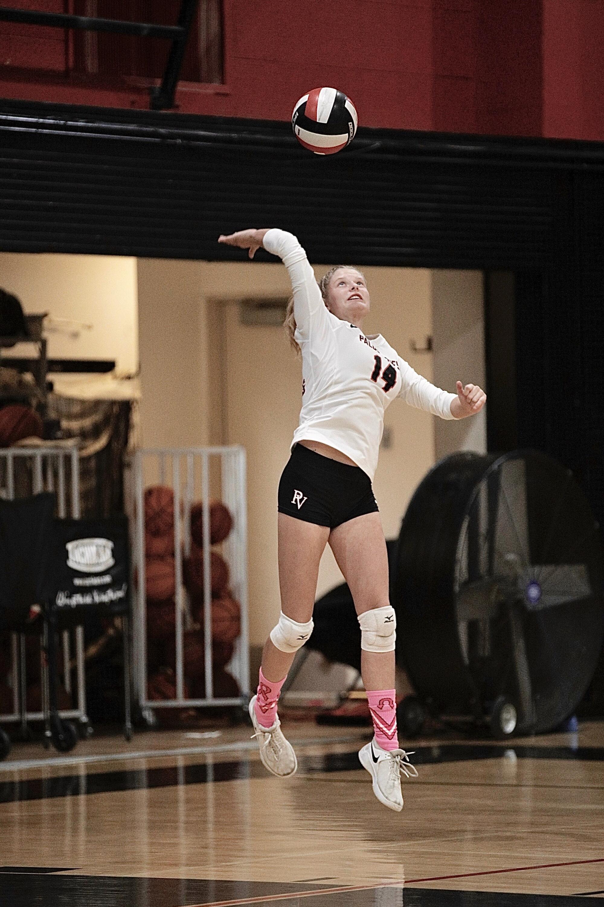 A girl leaps up to hit a volleyball.