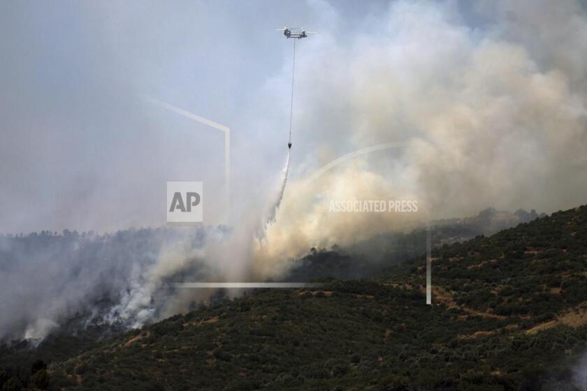 A helicopter drops water to extinguish a fire raging across a forested area in Odemis, near Izmir, Turkey, Friday, July 4, 2025. (Cengiz Malgir/Dia Photo via AP)