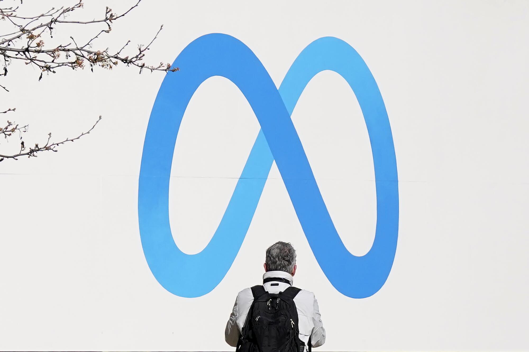 A person stands below blue infinity-shaped Meta logo 