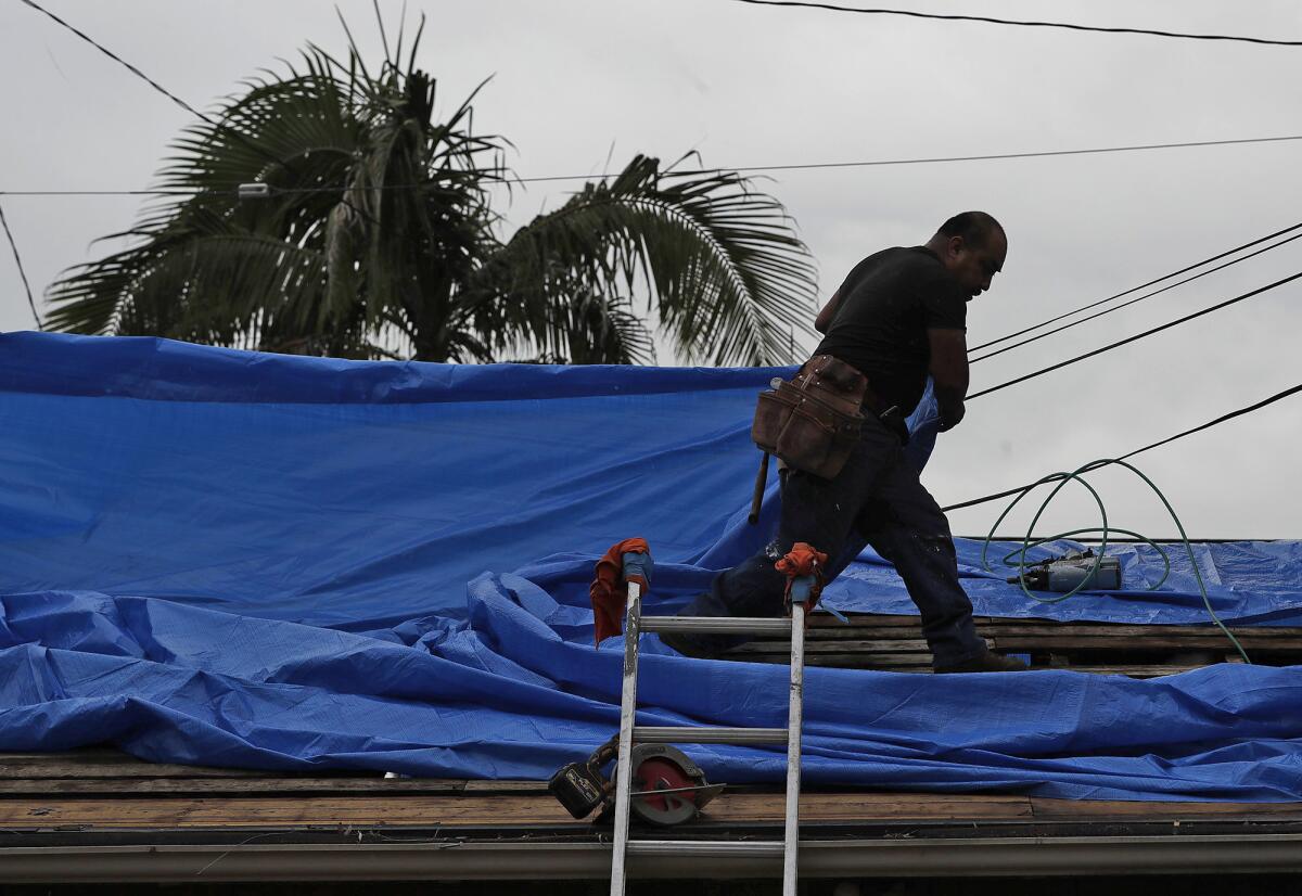 Construction worker John Torrez pulls a tarp over a roof as rain begins to fall on Friday in Laguna Beach.