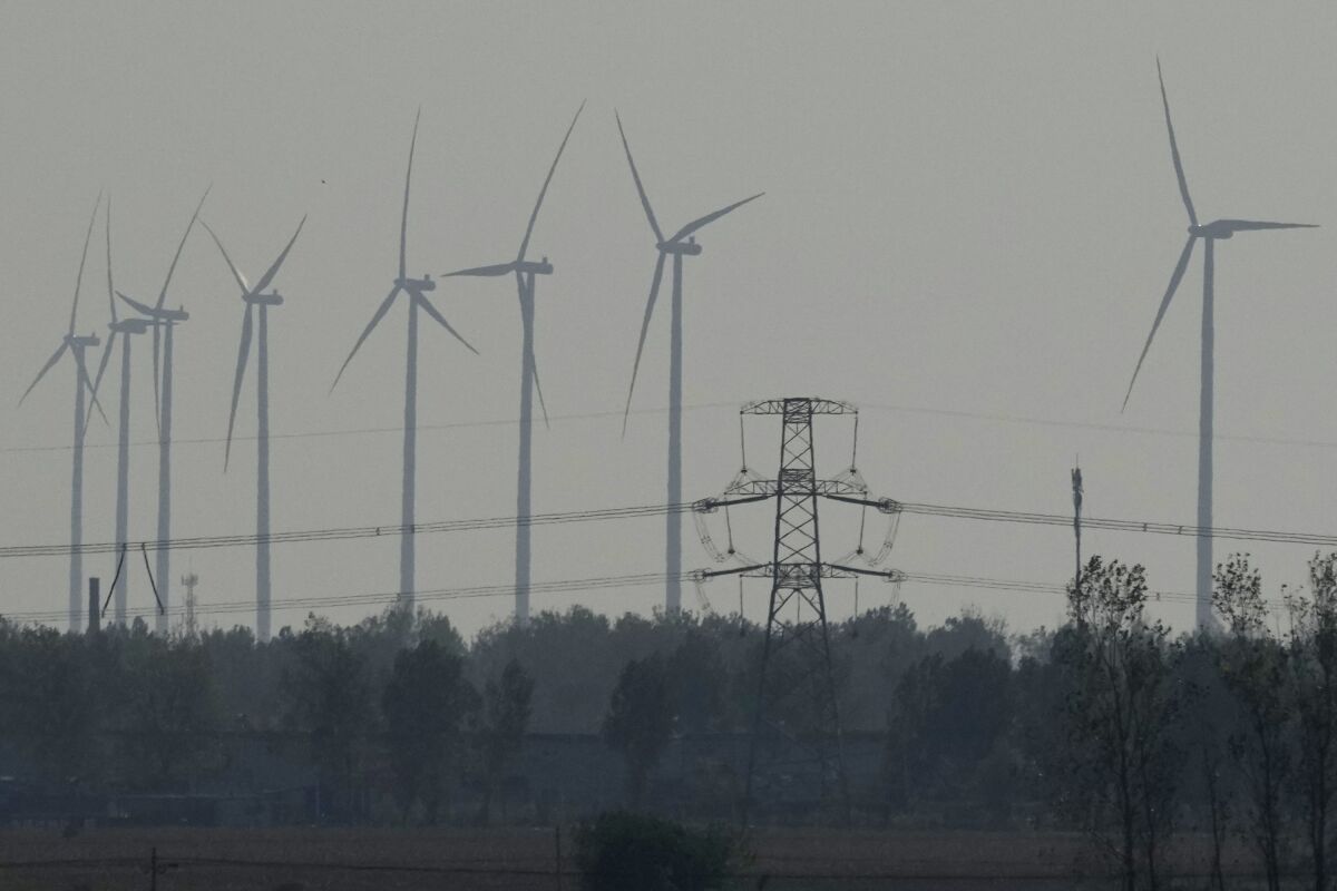 Wind turbines are seen near a power line near central China's Henan province on Friday, Oct. 22, 2021. China and U.S. had a "very good year" for collaboration on dealing with climate change, but Washington is still pushing Beijing to adopt more ambitious carbon reduction goals, the top U.S. diplomat in China said Friday, Dec. 10. (AP Photo/Ng Han Guan)