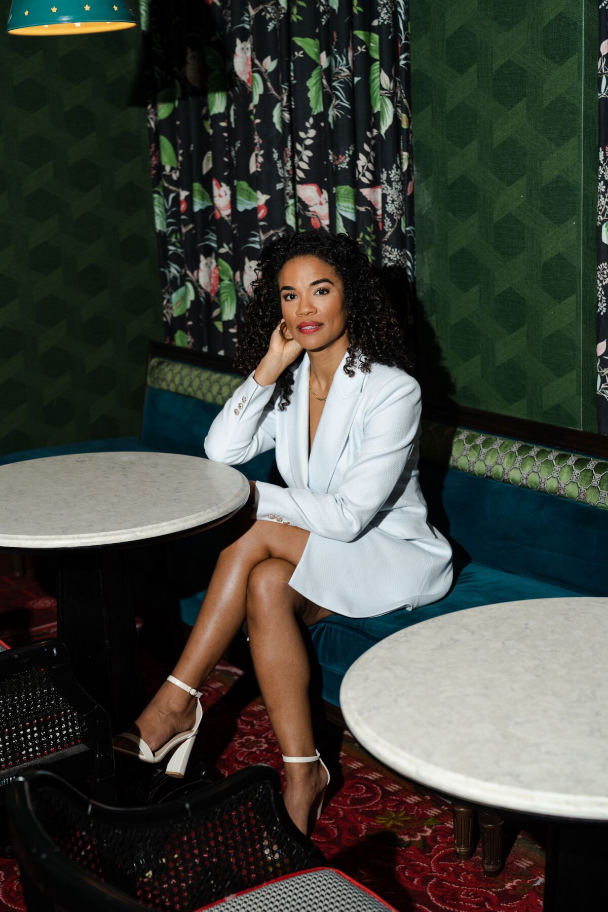 Britney Coleman in a white skirt suit sits behind a restaurant table.