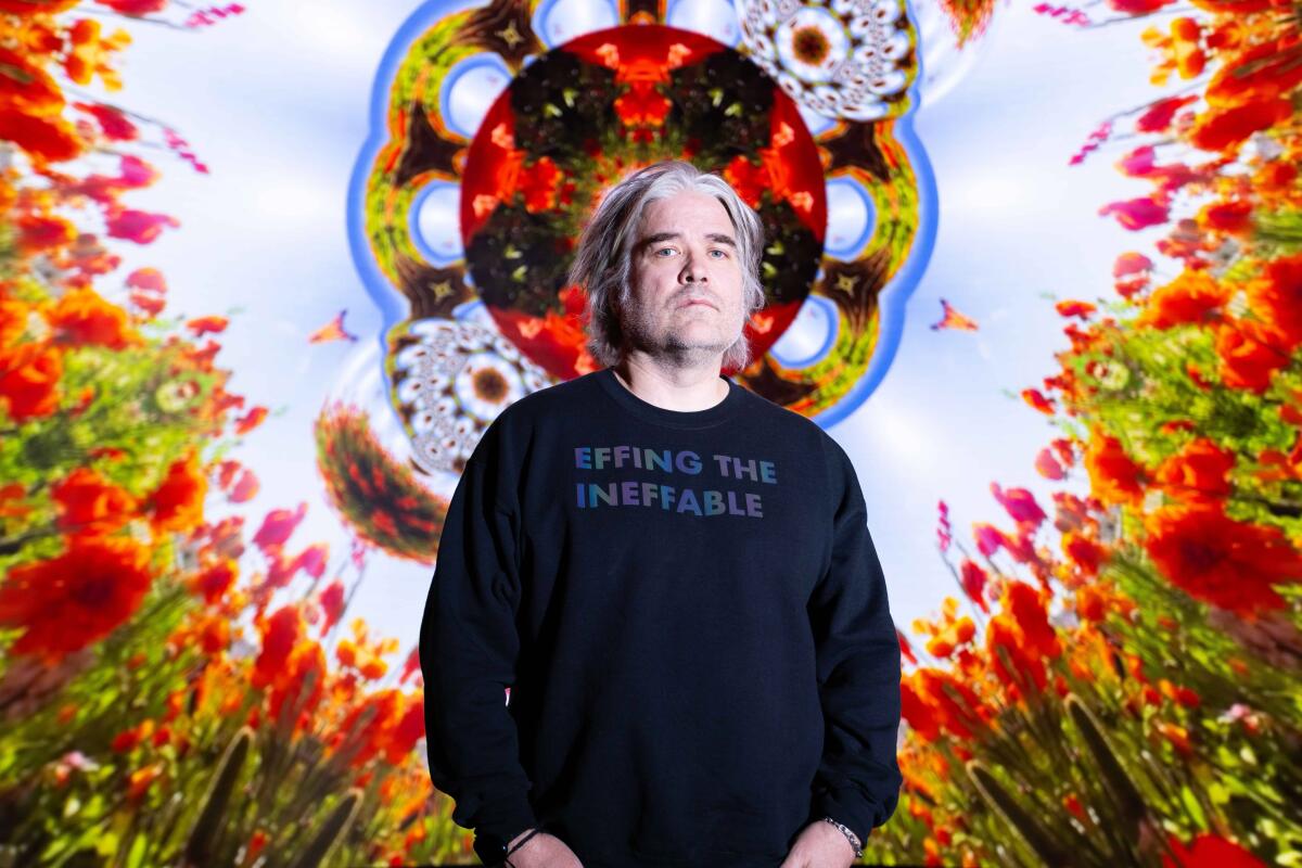 Artist Chris Holmes wears a navy sweatshirt and stands before his colorful kaleidoscopic art piece "The Journey Within."  