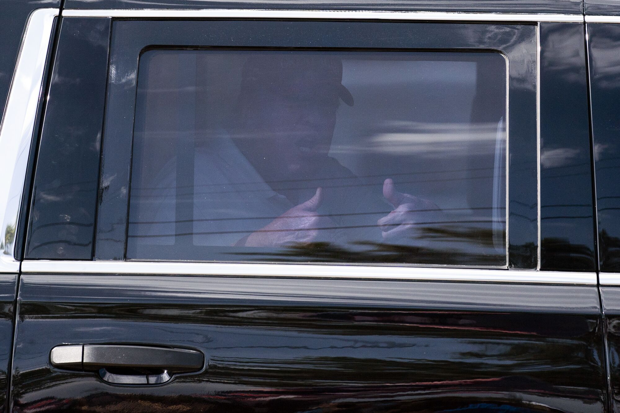 Kırmızı bir bere takan Donald Trump, bir arabanın arkasında giderken iki başparmağını kaldırıyor.