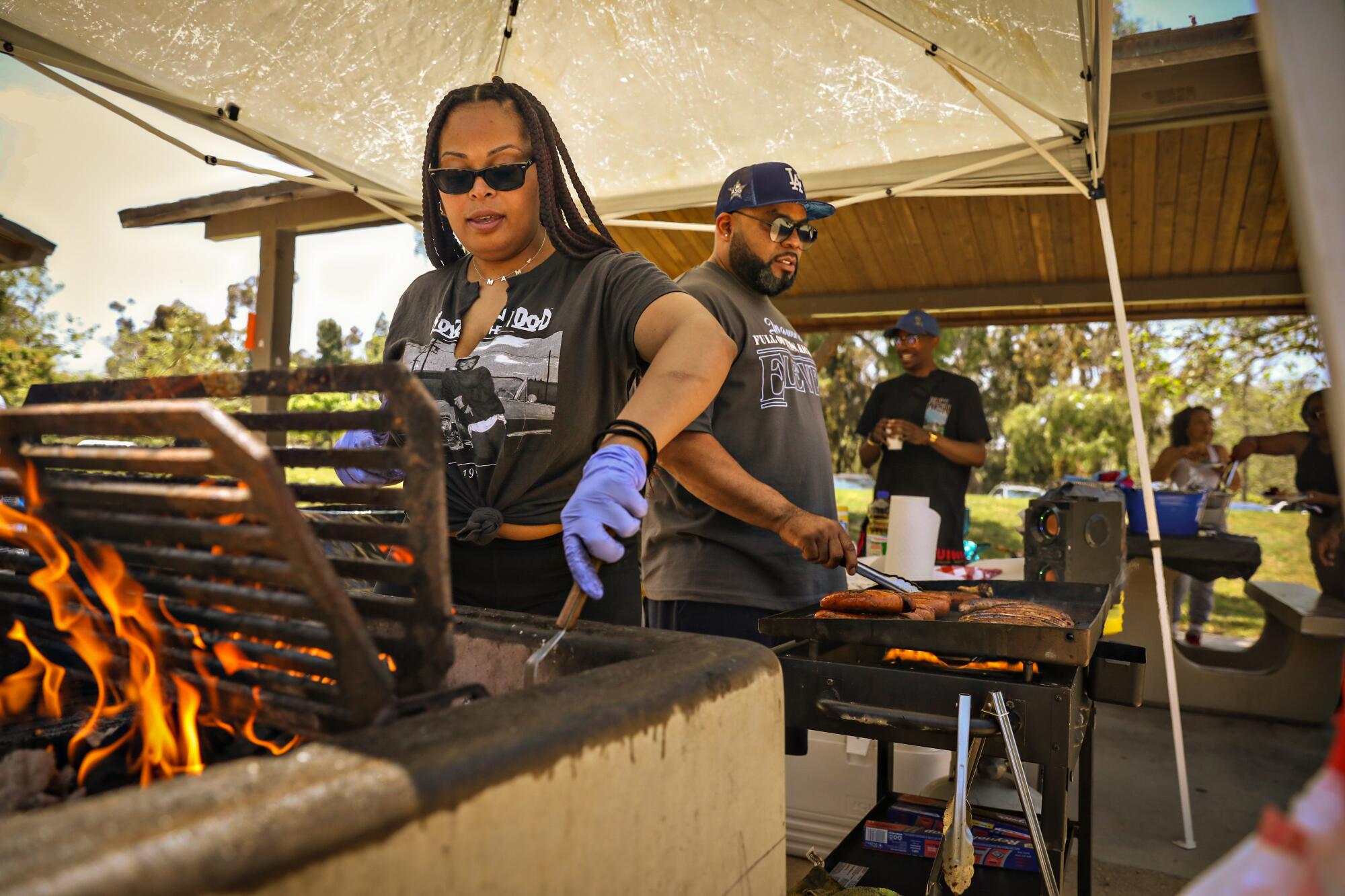 A woman and a man grill meat under a canopy.