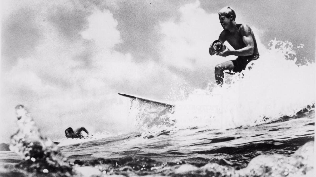 American surfer and director Bruce Brown surfs and holds a camera while filming footage for 'The Endless Summer.'