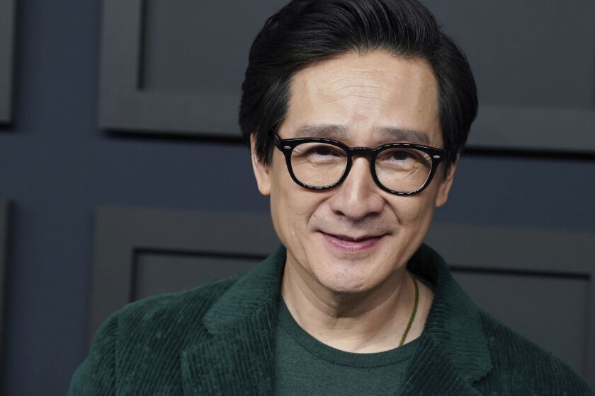 A man with short dark hair and thick black glasses in a dark green blazer smiling