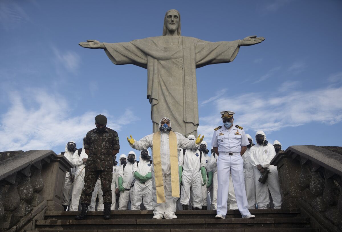 Catholic Priest Omar, center, leads a prayer as soldiers pause from disinfecting the Christ the Redeemer area, currently closed during the new coronavirus pandemic in Rio de Janeiro, Brazil, Thursday, Aug. 13, 2020. (AP Photo/Silvia Izquierdo)