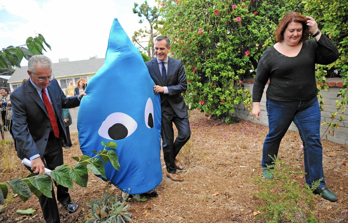 City Councilman Paul Krekorian, left, and Mayor Eric Garcetti guide a person in a water drop costume into the yard of homeowner Carrie Wassenaar, right, for a demonstration of a high-tech rainwater-capturing system.