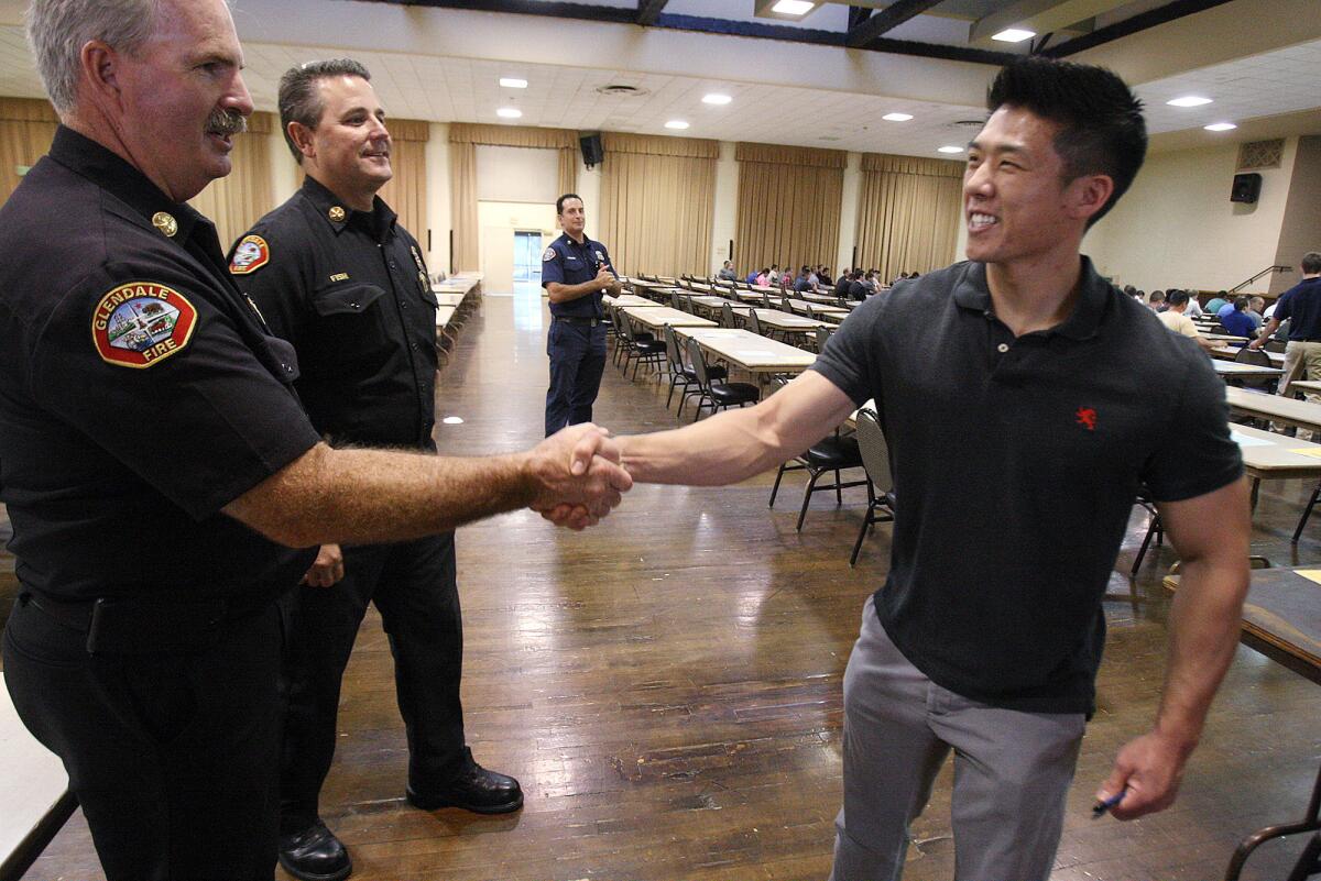 Stanley Woo, of Glendale, shakes hands with Battalion Chief Tom Propst and Battalion Chief Greg Fish as he enters the hall at the Glendale Civic Auditorium for a fire fighters examination on Tuesday, September 10, 2013. A couple hundred hopeful citizens, of over 1,800, took an exam as the first step to become one of 15 available positions in the Glendale Fire Department. This is Woo's first attempt at the test.