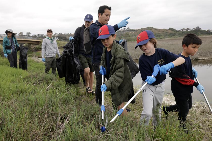 ENCINITAS, CA - APRIL 20, 2024: Daniel Sutoyo, a parent, points as he, Cub Scouts from Pack 734 and other parents pick up trash at the San Elijo Lagoon in Encinitas during the I Love a Clean San Diego's 22nd annual Creek to Bay Cleanup, a one-day event where thousands of volunteers work to remove trash at nearly a 100 sites across San Diego County to celebrate Earth Week on Saturday, April 20, 2024. (Hayne Palmour IV / For The San Diego Union-Tribune)