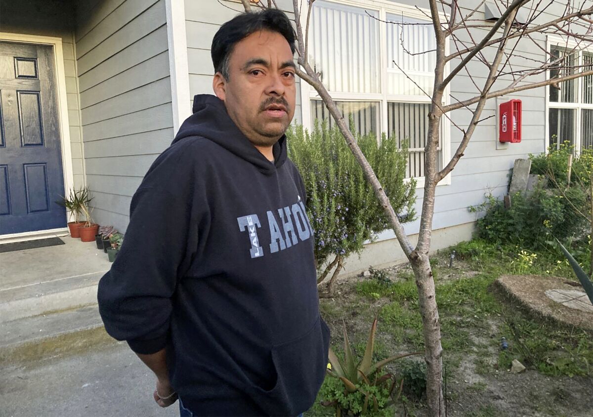 A man in a hooded sweatshirt stands outside of a house.
