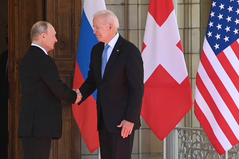 President Biden and Russian President Vladimir Putin shake hands in front of flags.