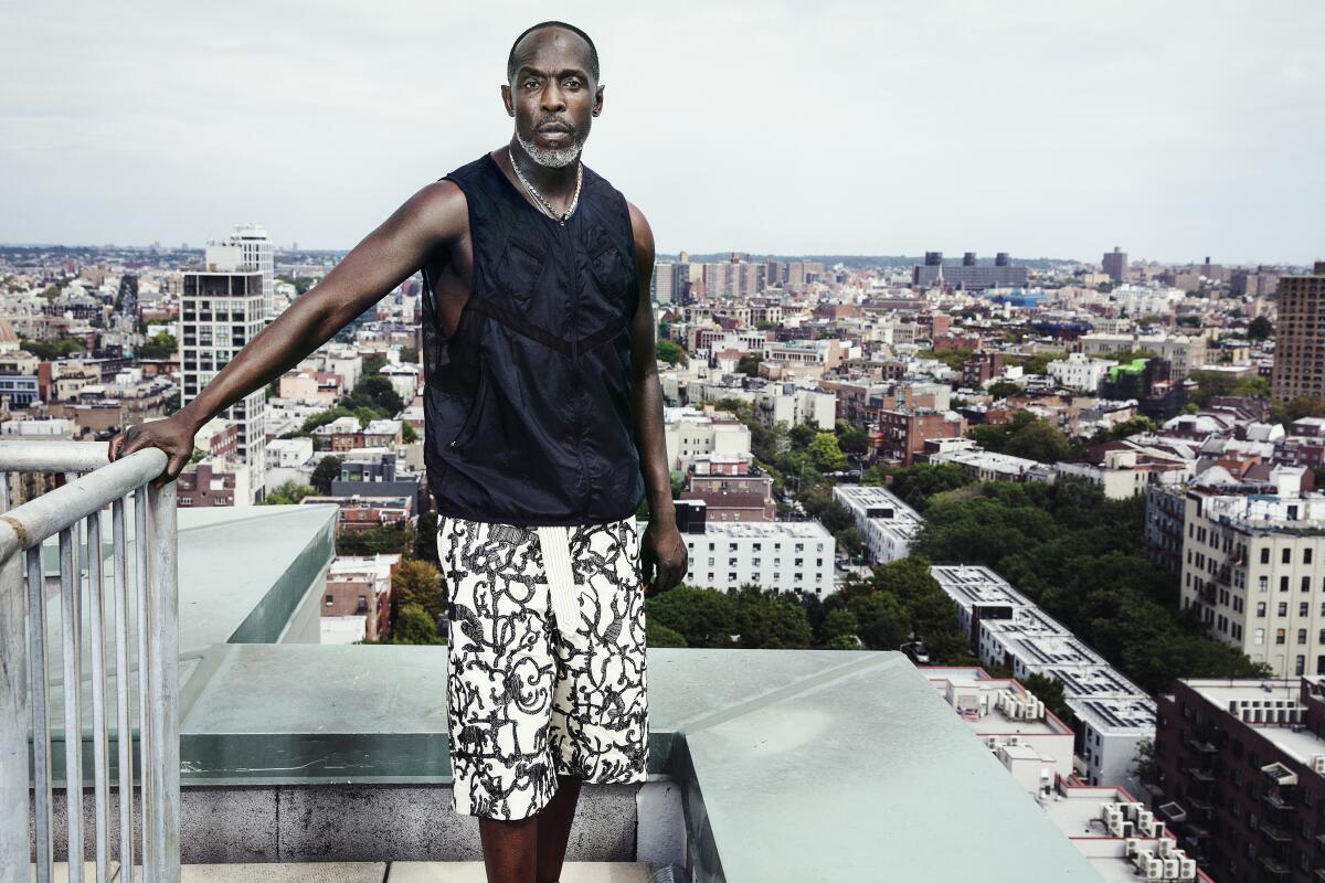 Michael K. Williams stands on a Brooklyn rooftop in black sleeveless tee and white patterned shorts.