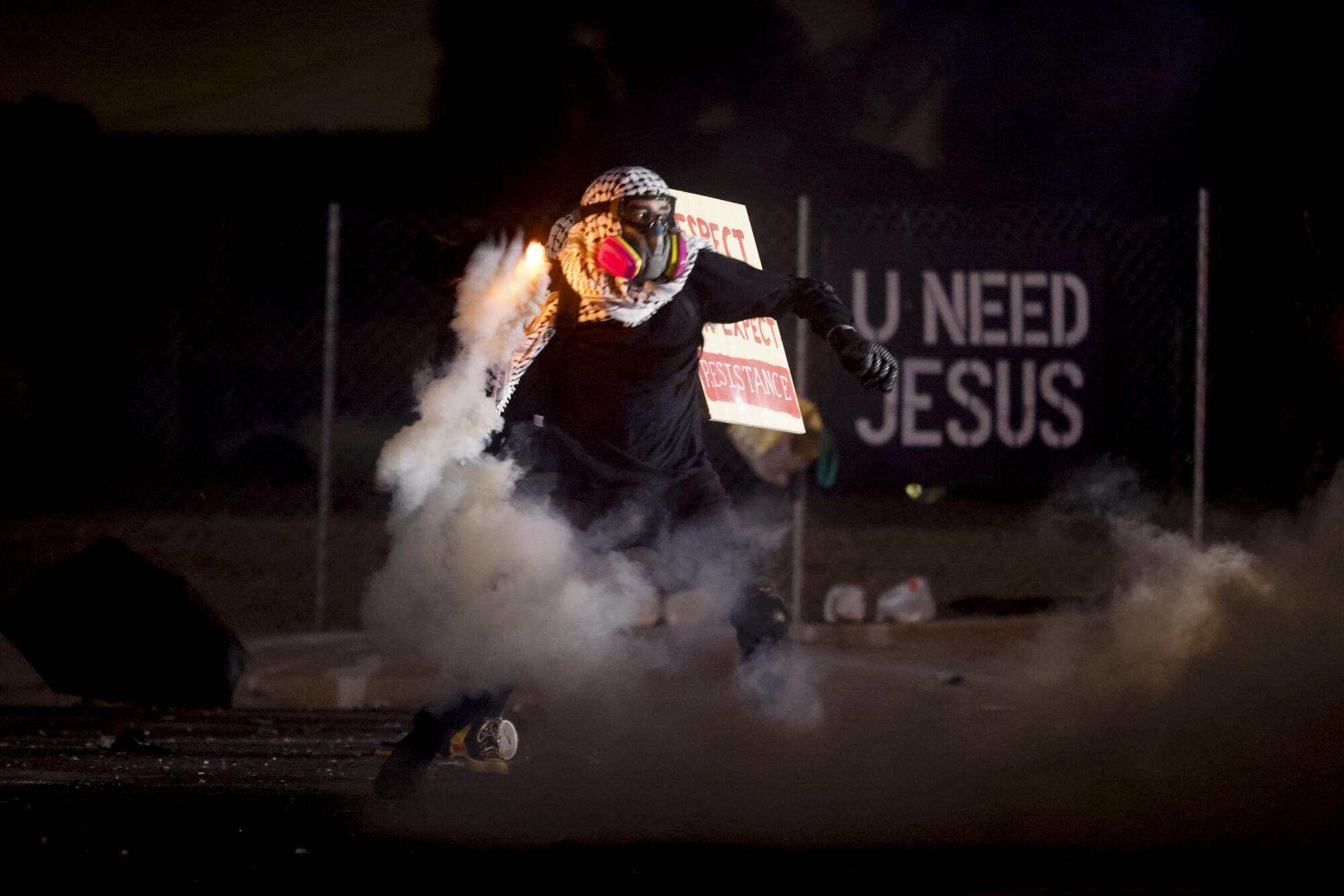 An anti-ICE protester throws back a tear gas canister.