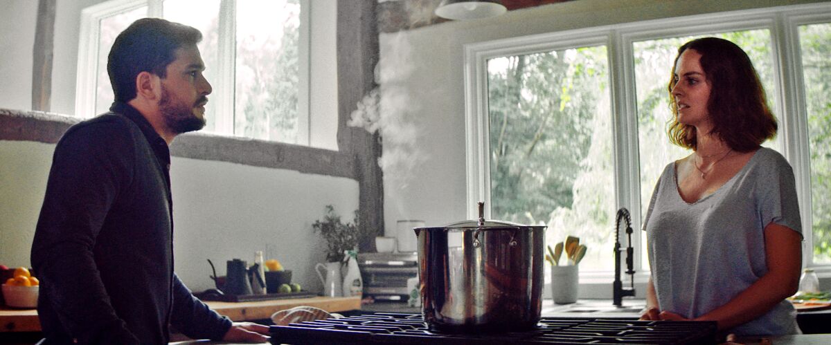 A man and woman stand opposite each other in a kitchen.
