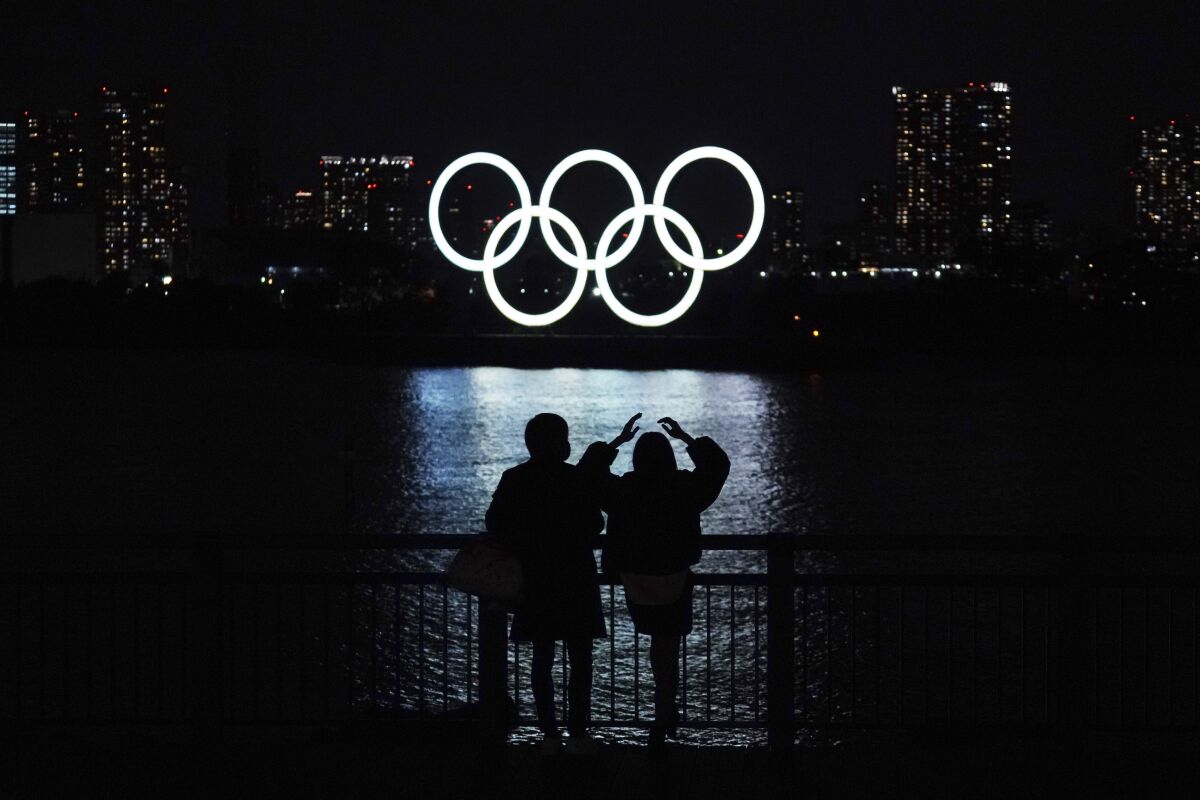 A man and a woman look at the Olympic rings float in the water in the Odaiba section Tuesday, Dec. 1, 2020, in Tokyo. The Olympic Symbol was reinstalled after it was taken down for maintenance ahead of the postponed Tokyo 2020 Olympics. (AP Photo/Eugene Hoshiko)