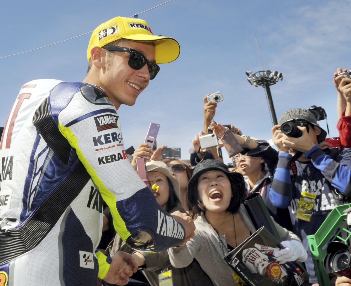 FILE - Italian MotoGP rider Valentino Rossi shakes hands with cheering fan after a free practice session of the Japan Motorcycle Grand Prix at Twin Ring Motegi circuit in Motegi, north of Tokyo, on Sept. 27, 2008. Record-breaking motorcycle racer. Charismatic showman. Italy's most popular athlete for years. Valentino Rossi was all that and more. He competed in his final race Sunday at the Valencia Grand Prix. He's the owner of nine world titles that include seven in the premier class. He's considered the greatest modern driver in his sport. (AP Photo/Katsumi Kasahara, File)