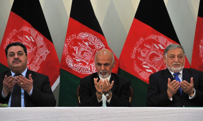 Afghan president-elect Ashraf Ghani, center, prays while flanked by Independent Electoral Commission chief Yousuf Nuristani, right, and deputy chief Abdul Rahman Hotaki at a ceremony in the commission's compound in Kabul on Sept. 26..
