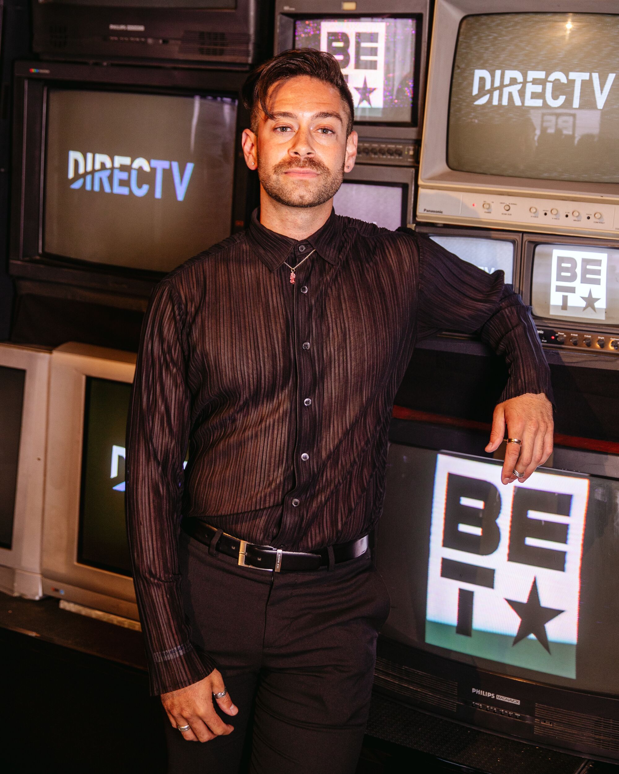 A man poses for a portrait in front of TVs.