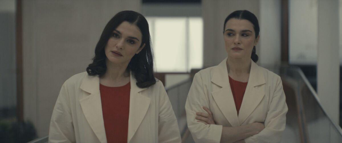 Twin doctors in lab coats and red shirts stand next to one another.