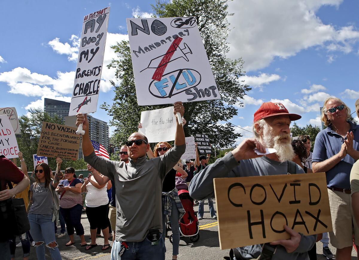 FILE - In this Aug. 30, 2020, file photo, Sal Lando, left, of Sterling, holds up signs during a protest against mandatory flu vaccinations, outside the Massachusetts State House, in Boston. Psychology experts offer several suggestions for talking to friends and family who believe conspiracy theories about COVID-19. Instead of lecturing or mocking, listen and ask them why they believe what they believe. (Nancy Lane/Boston Herald via AP, File)