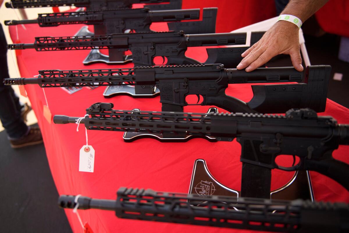 A row of AR-15-style rifles bearing price tags on a tabletop. 