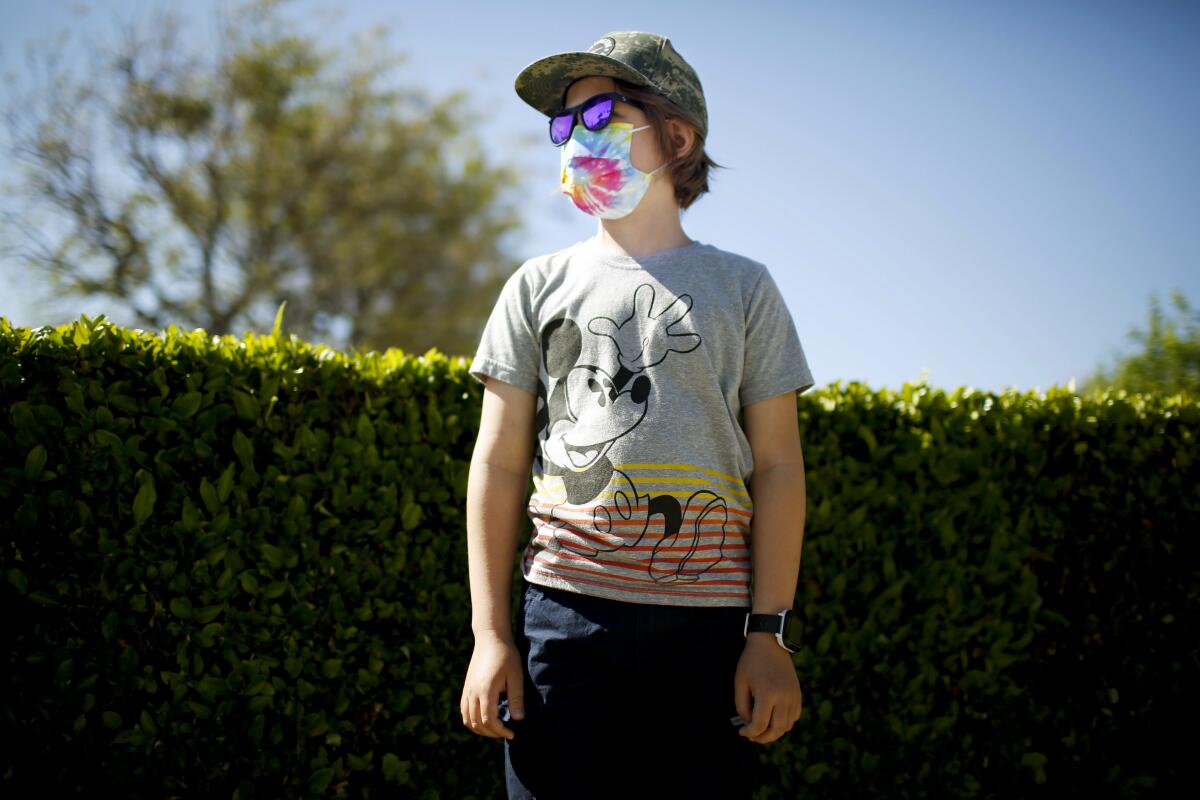 A boy in a Mickey Mouse shirt, tie-dye mask, sunglasses and camouflage hat