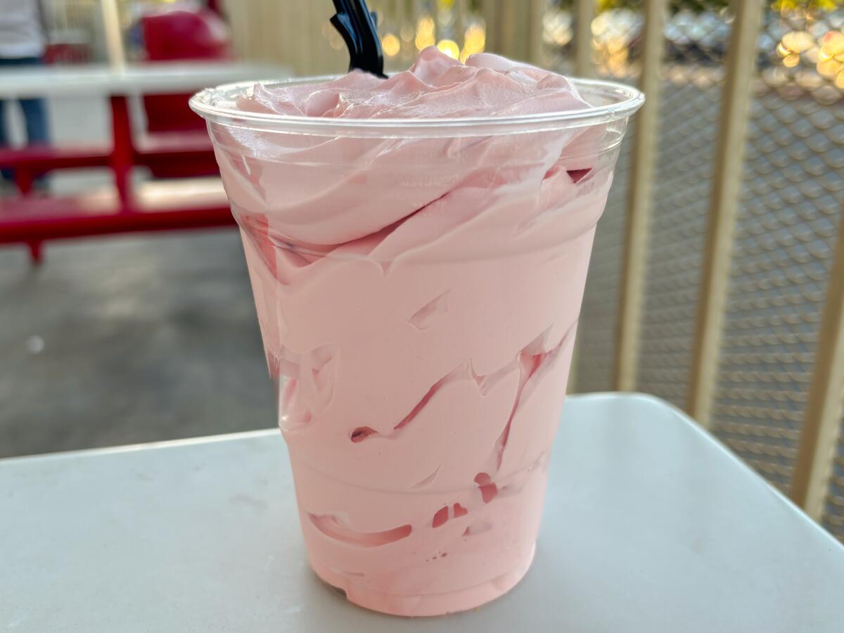 Pink ice cream in a clear plastic cup on a table.