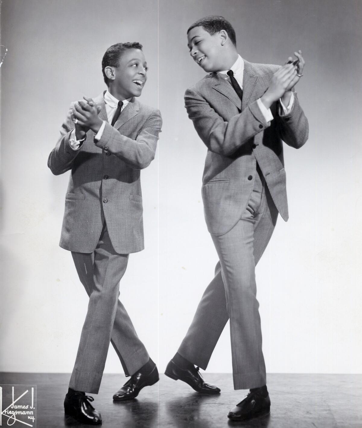 The young Hines brothers stand with hands clasped and feet in matching positions, looking at each other over one shoulder.