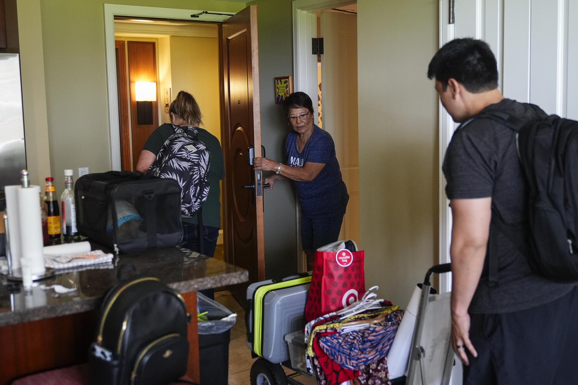 Leola Vierra holds open the door a young woman and man as they carry belongings out of a hotel room. 