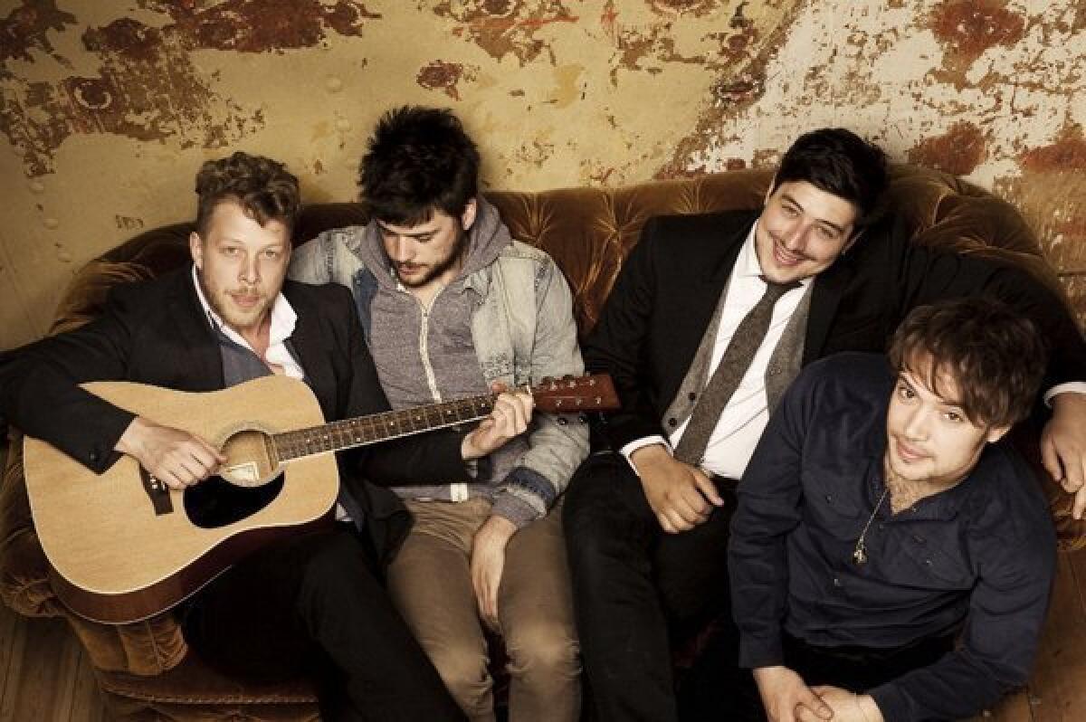 Mumford & Sons members sit on a couch with a guitar.