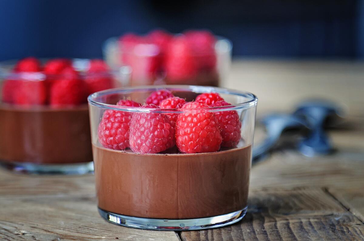 Glass dishes hold dark chocolate pots de creme with fresh raspberries.