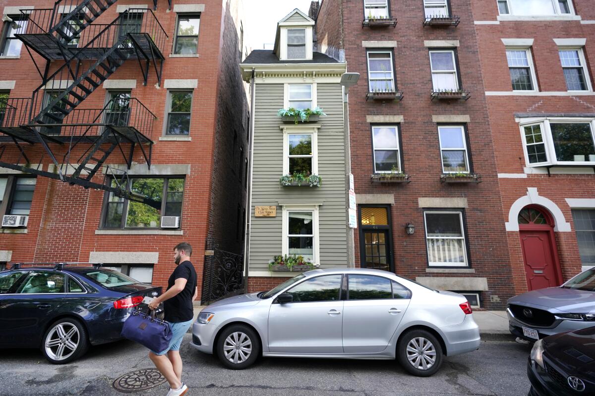 A man walks by Boston's famous Skinny House, middle, Friday, Aug. 13, 2021, which is on the market for $1.2 million. This is the first time the vertically rectangular-shaped house has been on the market since 2017 when it was sold for $900,000. The home, located in Boston's North End, is about 1,165 square feet and is barely 10 feet wide at its widest point. (AP Photo/Elise Amendola)