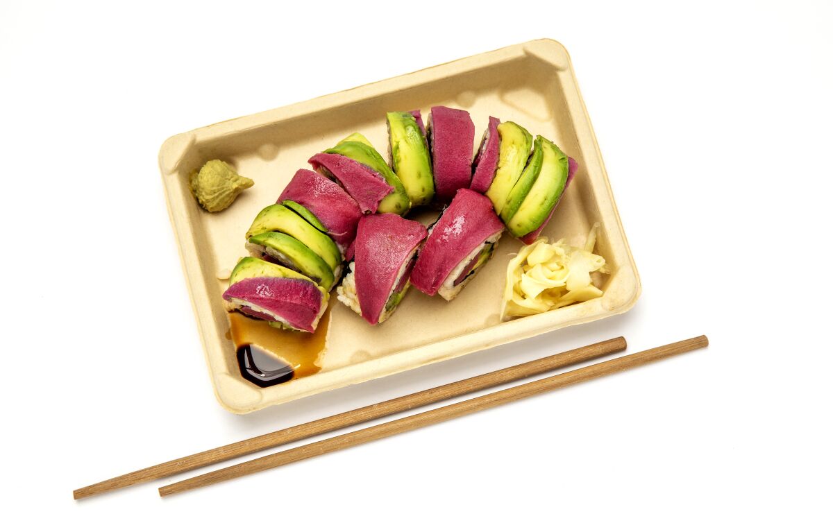 A to-go container with sliced sushi sits alongside a pair of chopsticks.