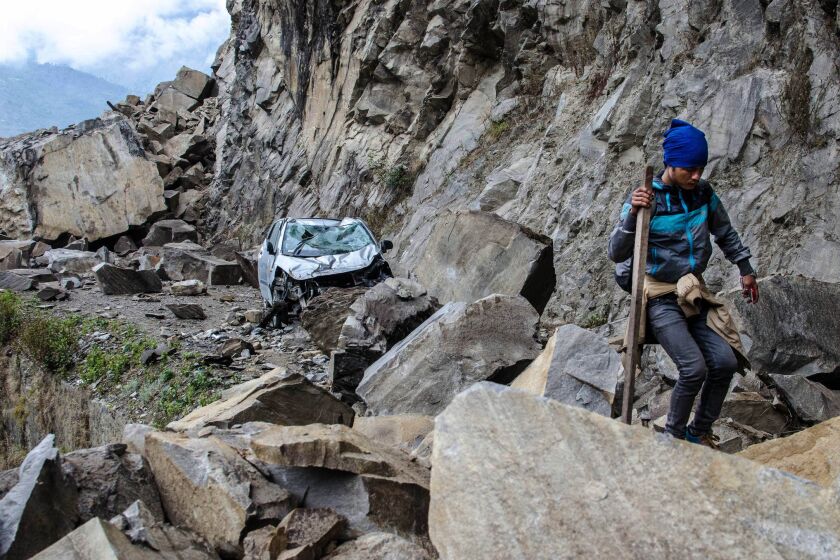 A Nepalese man walks over fallen rocks and past a crushed car on the way to a village in Langtang National Park.