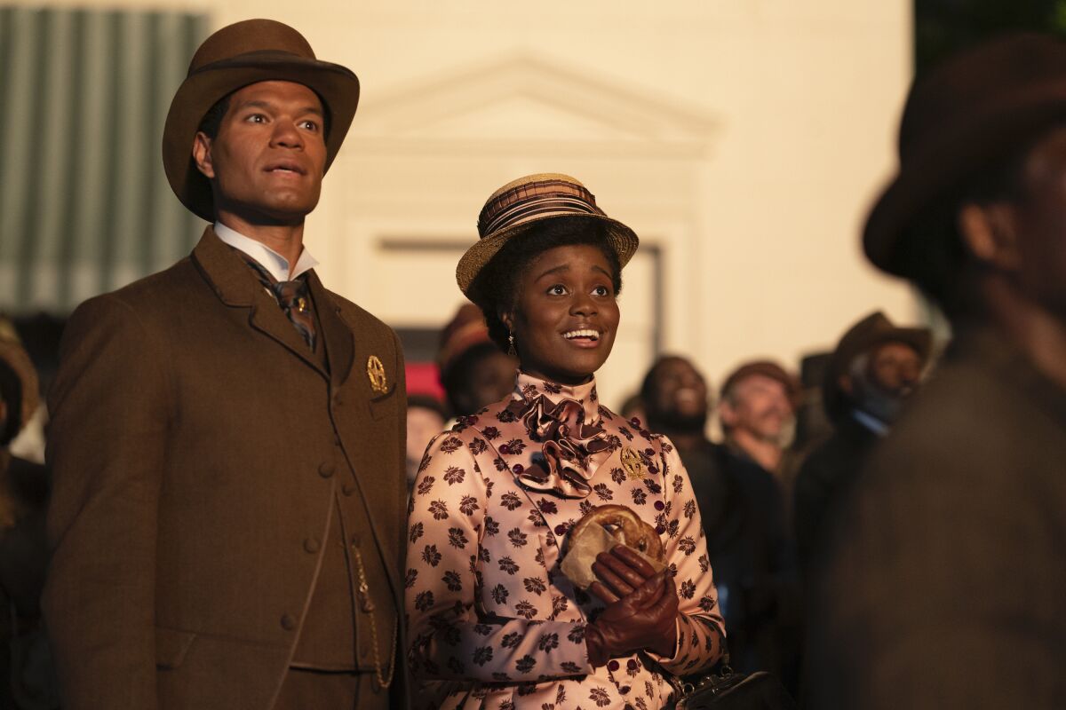 A man in a brown suit and a woman in a pink suit in a crowded public space