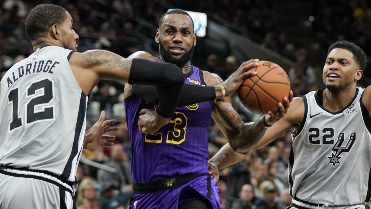 Lakers forward LeBron James drives to the basket between Spurs forwards LaMarcus Aldridge and Rudy Gay (22) during the first half Friday night.