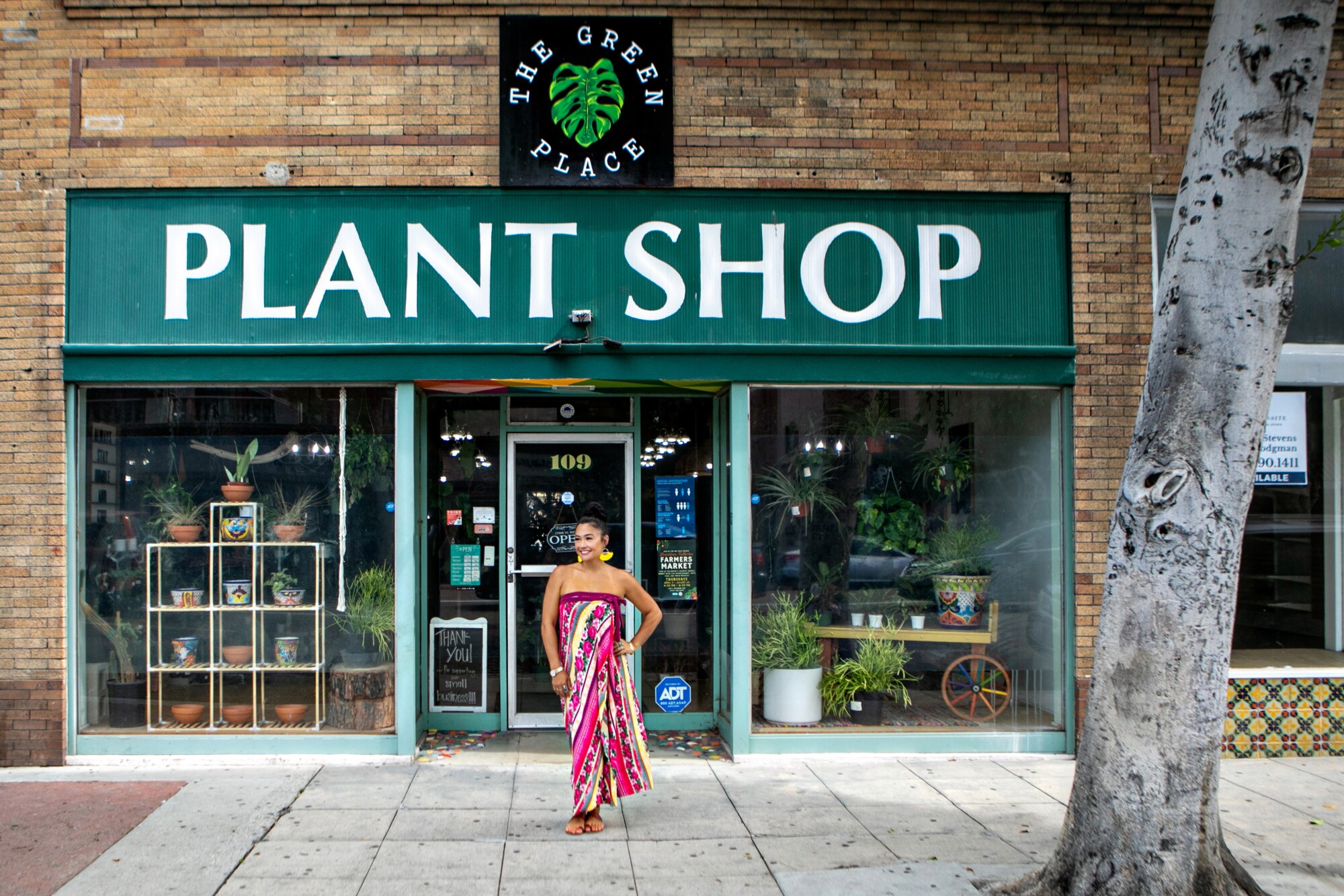 A woman stands outside a store reading a sign on the sidewalk "Green Place Plant Shop."